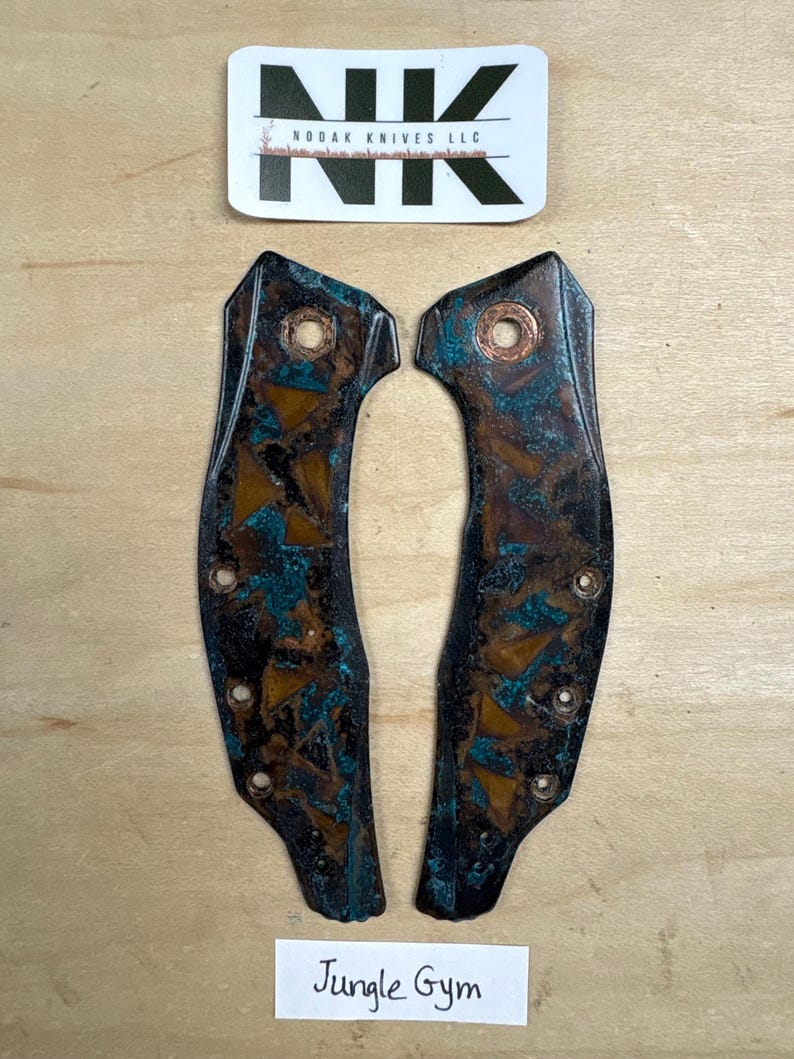 May include: Two knife handle scales with a brown and teal patina. The scales have multiple holes for attachment and a copper rivet. The top of the image has a sticker with the text "NK" and "NODAK KNIVES LLC". The bottom of the image has the text "Jungle Gym".