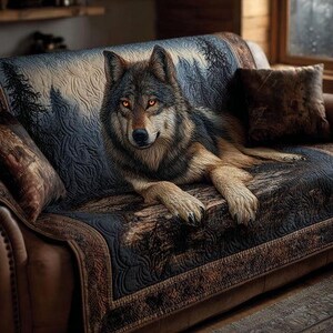 May include: A detailed image of a wolf with orange eyes resting on a sofa. The sofa has a patterned cover with a forest scene. The wolf's fur is a mix of brown, black, and tan. Two throw pillows are on the sofa.