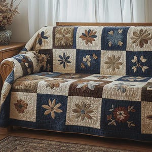 Puede incluir: Una funda de sofá acolchada con un diseño de patchwork con motivos florales. Los cuadrados alternan entre crema, azul marino y marrón, con flores bordadas en varios colores. La funda está colocada sobre un sofá de madera.