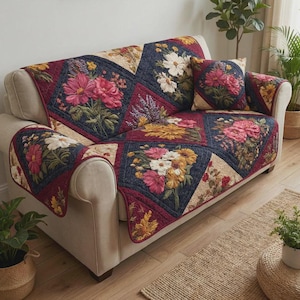 May include: A floral quilted sofa cover and matching cushion set. The cover has a patchwork design with large, colourful flower bouquets in shades of pink, white, and yellow against a navy blue background. The sofa is beige.
