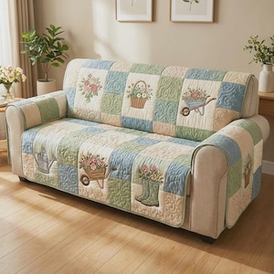 May include: A pastel-coloured, quilted sofa cover with a patchwork design. It features embroidered garden-themed motifs, such as flowers in baskets, wheelbarrows, and watering cans. The cover is designed to fit over a sofa.