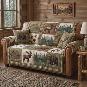 May include: A brown leather sofa with a patchwork quilt cover featuring cabin, bear, elk, and mountain scenes. Two matching throw pillows with bear and elk designs. The sofa is in a rustic, cabin-themed living room.