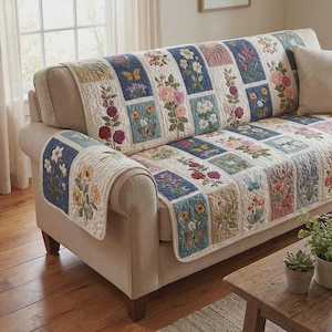Puede incluir: Una funda de sofá acolchada con estampado floral y diseño patchwork. La funda presenta cuadrados bordados con varias flores y mariposas en tonos rosa, azul, amarillo y verde. La funda está colocada sobre un sofá beige.