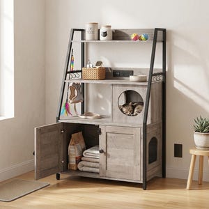 May include: A grey wood-effect cat furniture tower with a black metal frame, featuring an open top shelf, a middle shelf with a cat cubby and power outlet, and a lower cabinet with two doors containing folded blankets and a bag of pet food.