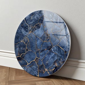 May include: A circular wall art piece featuring a deep blue marble pattern with intricate gold veining throughout. The surface has a glossy, reflective finish that highlights the fractured stone design, creating a striking contrast between the dark blue tones and the metallic gold lines.