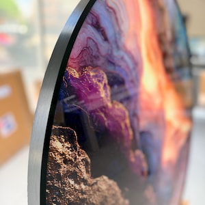 Side view close-up of tempered round glass wall art, black edge and glittering gold vein, purple orange geode tones