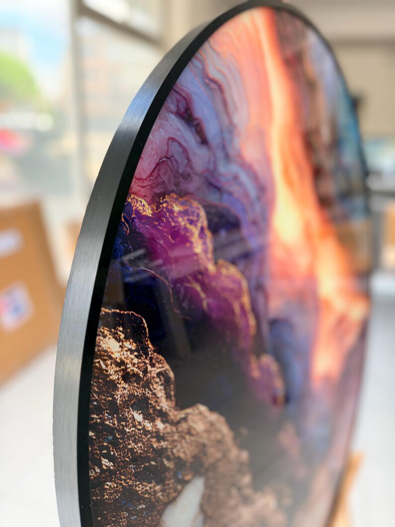 Side view close-up of tempered round glass wall art, black edge and glittering gold vein, purple orange geode tones