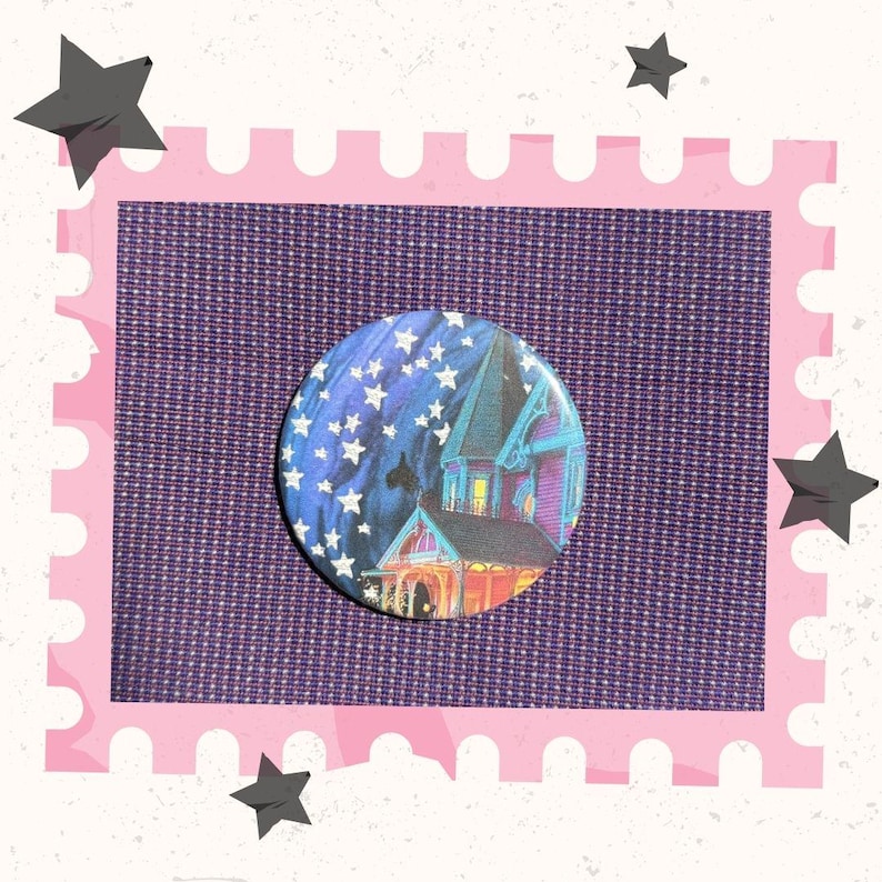May include: A round button with a spooky house illustration under a starry night sky. The house is purple and blue with orange and yellow lights in the windows. The button is on a purple textured background with a pink border and star accents.