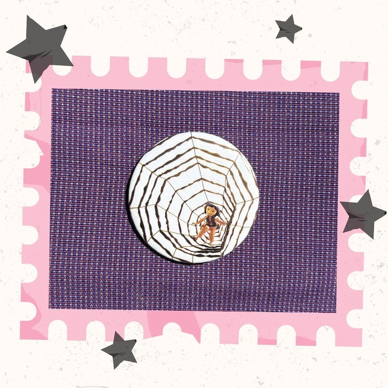 May include: A white button with a black and gold spiderweb design and a small figure in the center. The button is set against a purple background with a pink border and gray star accents.