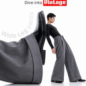 May include: Grey wide leg pants with a cuffed hem and a black long-sleeve shirt. The image features the text Dive into Vintage and Wide Leg pants. A large black leather shoe is positioned in the foreground against a white background.