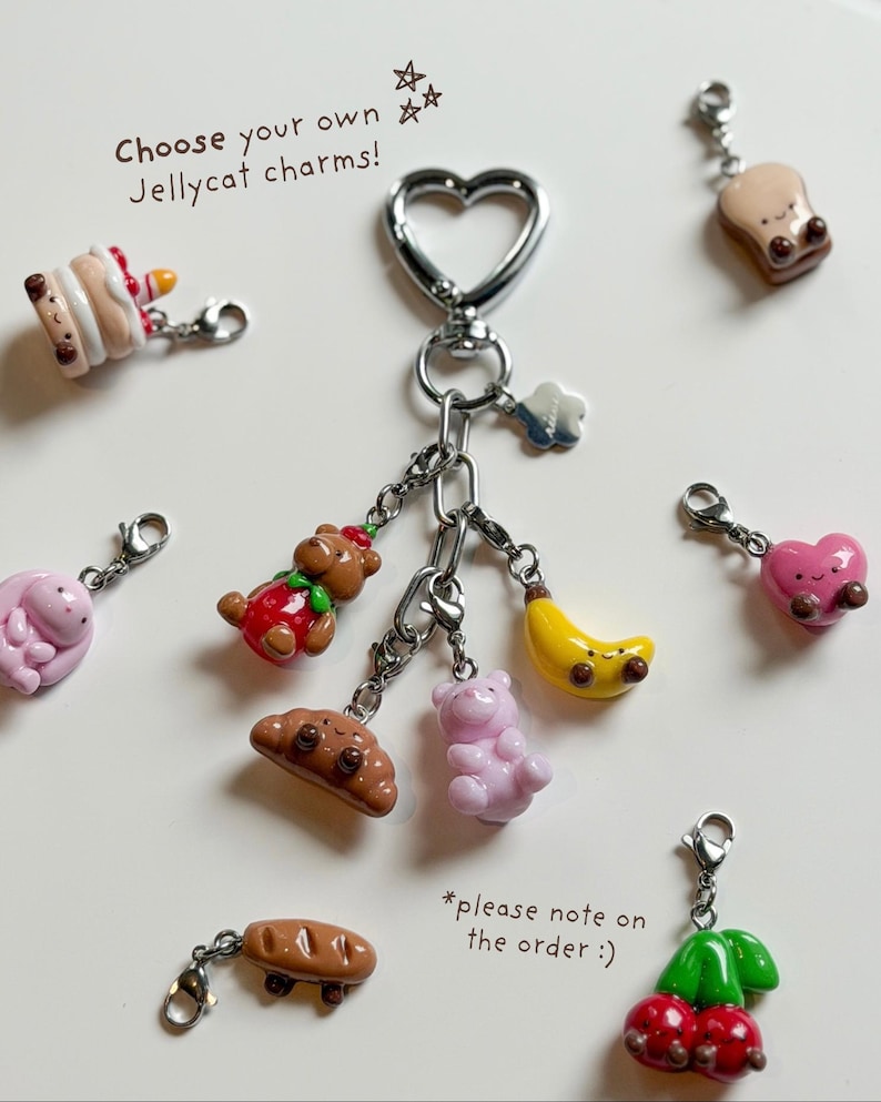 May include: A collection of Jellycat charms, including a cake, bear, croissant, banana, pink bear, bread, heart, and cherries. The charms are attached to a silver heart-shaped keychain. Text on the image reads "Choose your own Jellycat charms!"