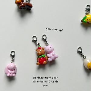 May include: A collection of colorful bear and bunny charms with silver clasps. One brown bear charm, a pink bunny charm, and a strawberry bear charm are visible. Text reads "new line up!" and "Bartholomew bear strawberry & Leola bear".