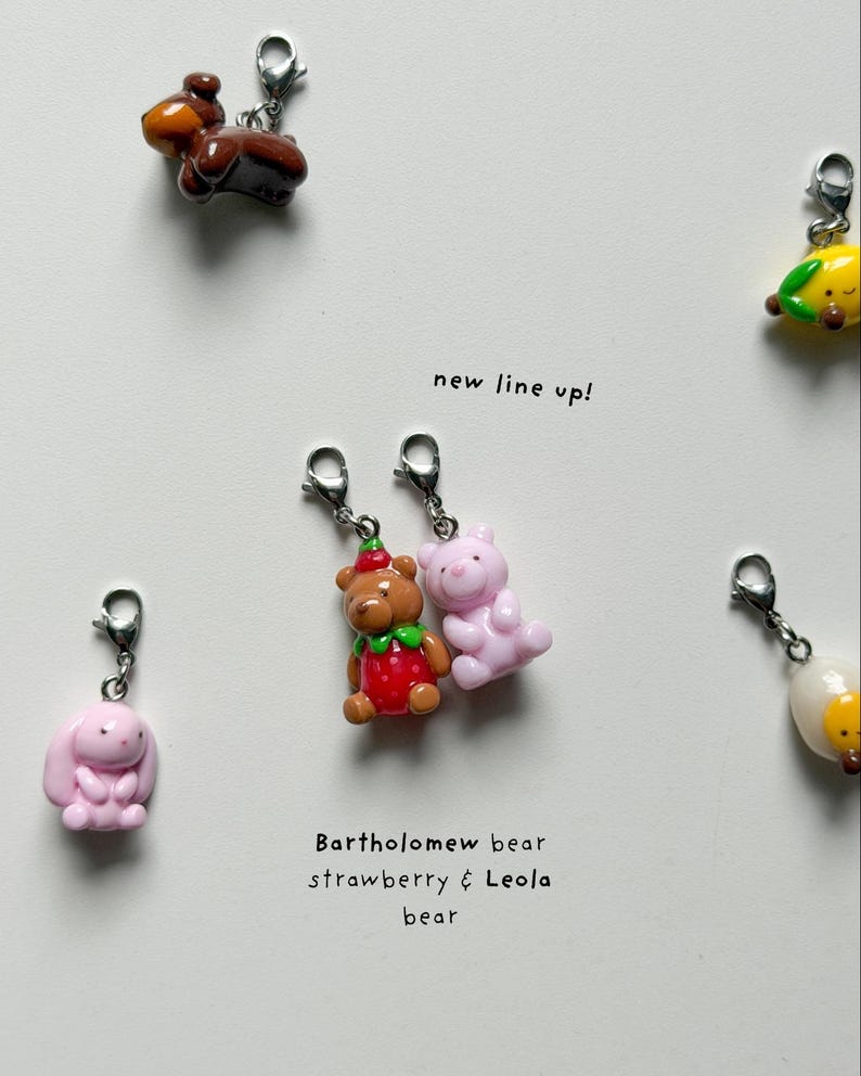 May include: A collection of colorful bear and bunny charms with silver clasps. One brown bear charm, a pink bunny charm, and a strawberry bear charm are visible. Text reads "new line up!" and "Bartholomew bear strawberry & Leola bear".