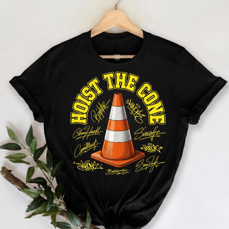 Op de afbeelding: Zwart T-shirt met een afbeelding van een oranje en witte verkeerskegel. De tekst "HOIST THE CONE" is geel. Het ontwerp bevat handtekeningen rond de kegel.