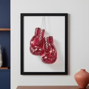 Può includere: Opera d'arte incorniciata con due guantoni da boxe rosso rubino sfaccettati sospesi a una catena d'argento. I guantoni hanno lacci bianchi e sono appesi su uno sfondo bianco all'interno di una cornice nera. Un pezzo decorativo per gli appassionati di sport.