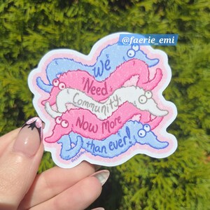 May include: A sticker featuring a design of colorful cartoon worms in pink, blue, and white. The sticker has the text "We Need Community Now More than ever!" and the Instagram handle "@faerie_emi".
