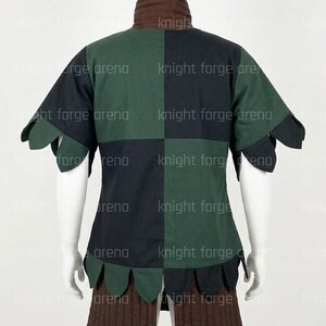 Peut inclure: Une tunique &agrave; manches courtes avec un motif &agrave; carreaux vert fonc&eacute; et noir. Le v&ecirc;tement poss&egrave;de un col haut marron et un ourlet festonn&eacute; le long des manches et du bas. Le texte knight forge arena est visible sur le tissu.