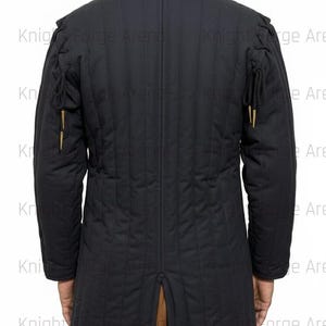 May include: Black quilted jacket with a high collar and vertical stitching. The jacket features decorative gold-colored accents on the sleeves and a split at the back hem. The text "Knight Forge" is visible in the background.