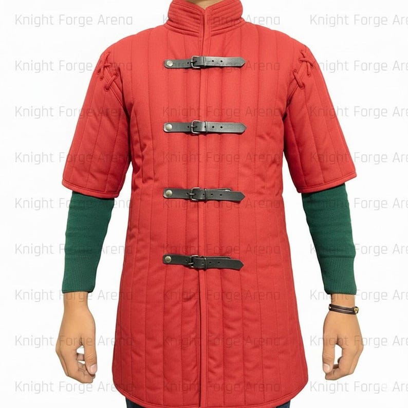May include: Red quilted gambeson with short sleeves and a stand-up collar. The medieval garment features black leather straps with buckles down the front. Green sleeves are visible underneath.
