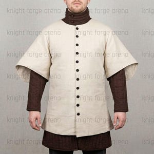 May include: A cream-colored medieval tunic with a high collar and long sleeves. The tunic features a button-down front with black buttons and is layered over a brown quilted undergarment. The text "knight forge arena" is visible.