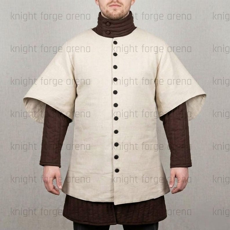 May include: A cream-colored medieval tunic with a high collar and long sleeves. The tunic features a button-down front with black buttons and is layered over a brown quilted undergarment. The text "knight forge arena" is visible.