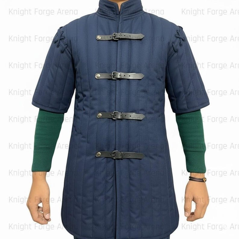 May include: A navy blue padded gambeson with short sleeves and a stand-up collar. The front closure features three black leather straps with buckles. The garment has vertical quilted stitching and is designed for historical reenactment or costume use.
