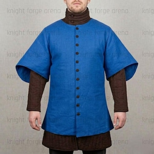 May include: A blue tunic with short, wide sleeves and a button-up front. The tunic is worn over a brown, quilted undergarment. The model is wearing a brown turtleneck. The text "knight forge arena" is visible in the background.