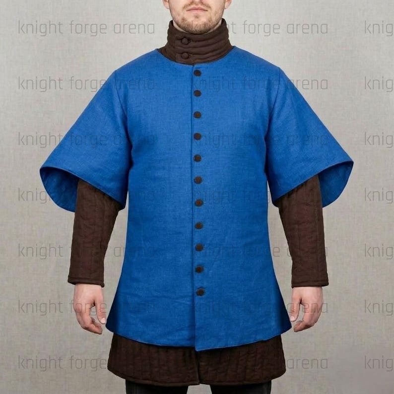 May include: A blue tunic with short, wide sleeves and a button-up front. The tunic is worn over a brown, quilted undergarment. The model is wearing a brown turtleneck. The text "knight forge arena" is visible in the background.