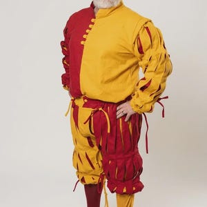 Peut inclure: Un pourpoint rouge et jaune &agrave; col montant et fermeture boutonn&eacute;e, associ&eacute; &agrave; une culotte fendue assortie avec des d&eacute;tails &agrave; nouer. La tenue comprend un b&eacute;ret rouge et jaune coordonn&eacute; ainsi que des bas unis de couleur rouge et jaune.