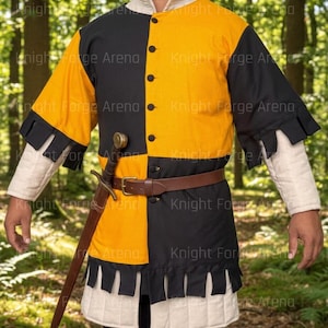 Può includere: Una tunica medievale nera e gialla, con cintura in pelle marrone e spada. La tunica ha orlo e maniche trapuntate. Il testo "Knight Forge Arena" è visibile.