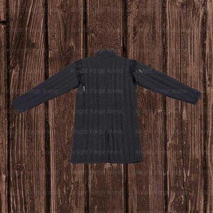 May include: A black quilted gambeson, a padded garment worn under armor. The long-sleeved jacket has a high collar and a buttoned front. The text "Knight Forge Arena" is visible on the garment.