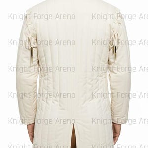 May include: Cream-colored, quilted jacket with a high collar and long sleeves. The jacket features vertical stitching and decorative ties on the shoulders and sleeves. The back of the jacket has a split at the hem. The text "Knight Forge Arena" is watermarked across the image.