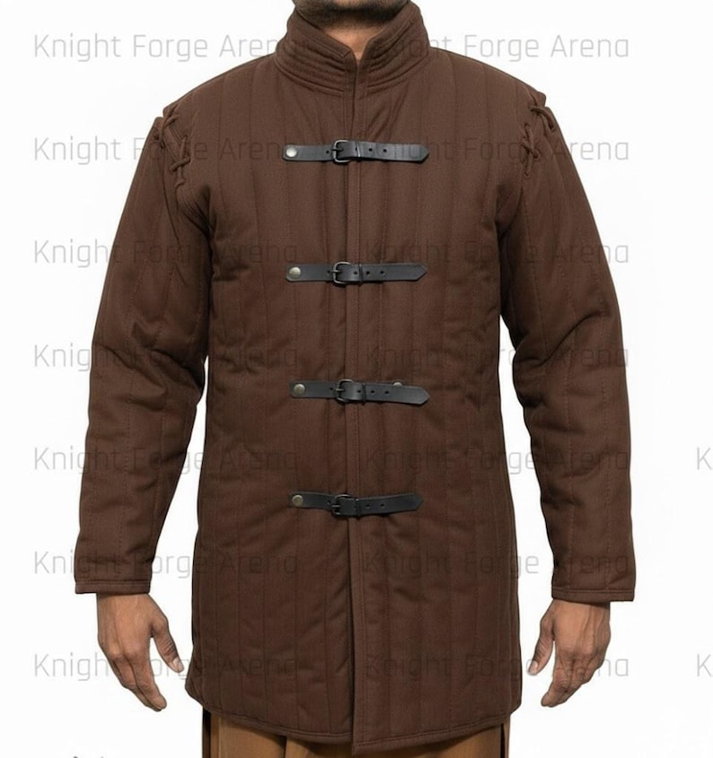 May include: Brown quilted jacket with black leather straps and buckles. The jacket has a high collar and long sleeves. The text "Knight Forge Arena" is visible in the background. This garment is suitable for historical reenactment or costume.