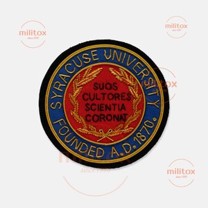 May include: A circular embroidered patch featuring the Syracuse University seal. The design includes a red center with gold wheat stalks and the Latin text Suos Cultores Scientia Coronat, surrounded by a blue border with gold lettering.