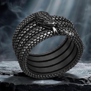 Peut inclure: Une bague en métal gris foncé en forme de serpent enroulé avec un motif d'écailles texturé recouvrant l'anneau. La tête du serpent présente une langue saillante et de petites pierres claires incrustées sur le côté du corps et dans les yeux.