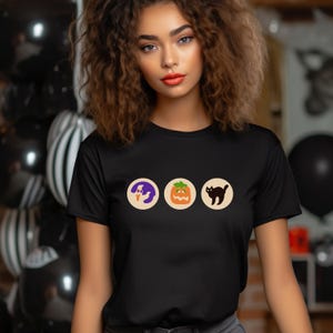 May include: A black t-shirt featuring a graphic of three Halloween icons: a ghost, a jack-o'-lantern, and a black cat.