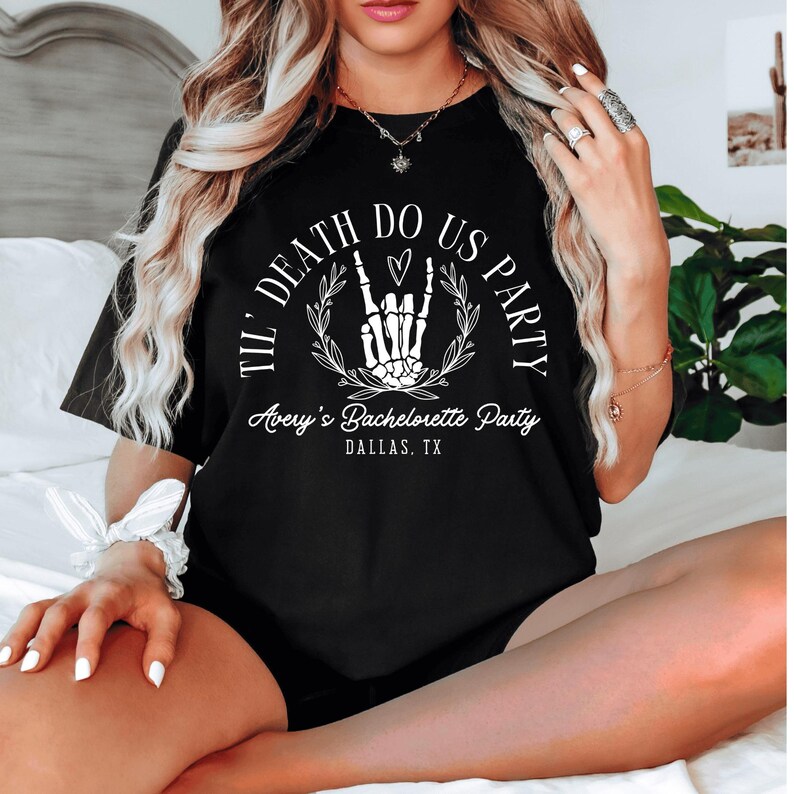 Puede incluir: Camiseta negra con texto blanco que dice "Til Death Do Us Party" con una mano de esqueleto haciendo un signo de rock and roll y un coraz&oacute;n. El texto "Avery's Bachelorette Party Dallas, TX" est&aacute; debajo del gr&aacute;fico.