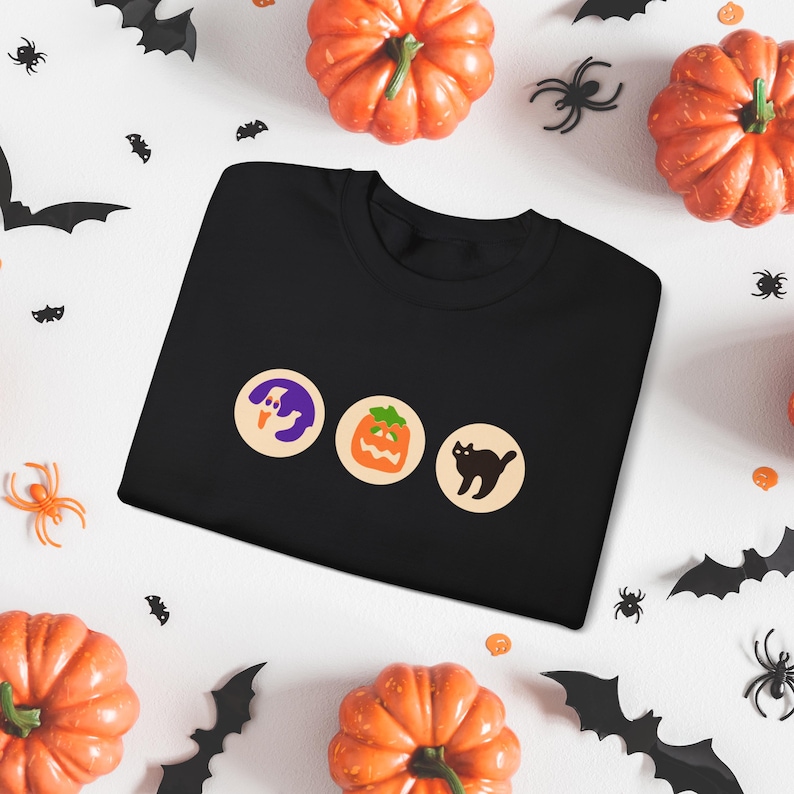 May include: Black t-shirt featuring three Halloween icons: a ghost, a jack-o'-lantern, and a black cat.