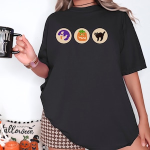 May include: Black oversized t-shirt with a graphic of a ghost, pumpkin, and black cat. The text "Happy Halloween" is printed on a white banner below the graphic.