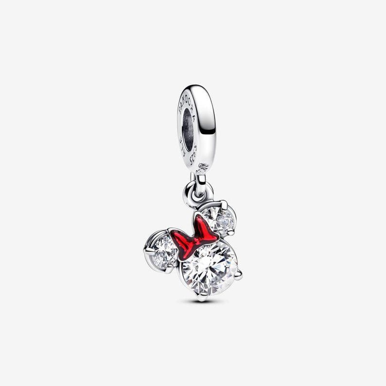 May include: A silver charm featuring a mouse-shaped silhouette with three clear round stones and a bright red enamel bow. The charm includes a circular bail engraved with the text PANDORA and S925, designed to hang from a bracelet or necklace chain.