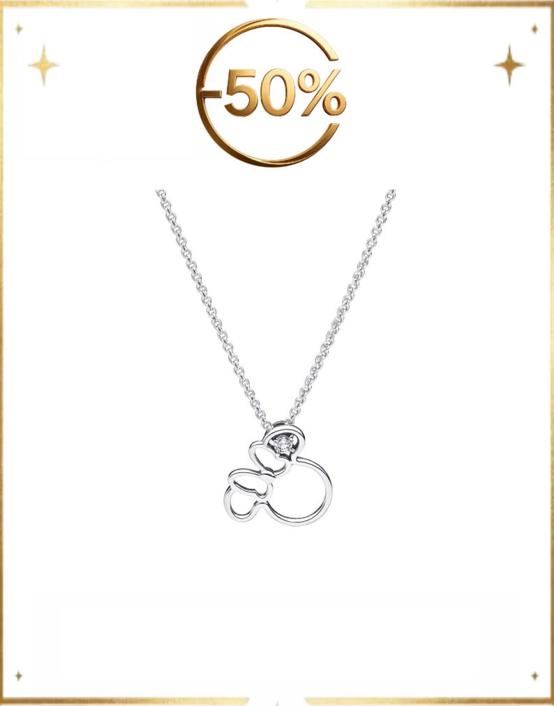 Op de afbeelding: Een zilverkleurige ketting met een hanger in de vorm van een gestileerde muizenkop met een strik, geaccentueerd door een kleine heldere steen. Boven de hanger toont een goudkleurige cirkelvormige afbeelding de tekst -50% op een witte achtergrond.
