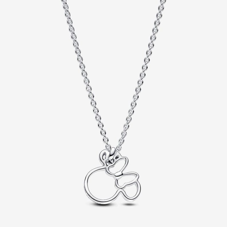 Op de afbeelding: Een zilverkleurige ketting met een hanger in de vorm van een gestileerd hoofd met een strik. De hanger is opgebouwd uit dunne, gepolijste metalen contouren en hangt aan een fijne, bijpassende zilverkleurige ketting met kleine, uniforme schakels.