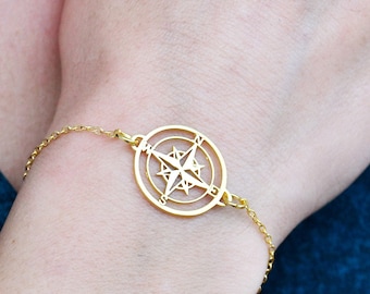 May include: A gold compass charm bracelet with a delicate chain. The compass charm is detailed with a north arrow and cardinal directions.
