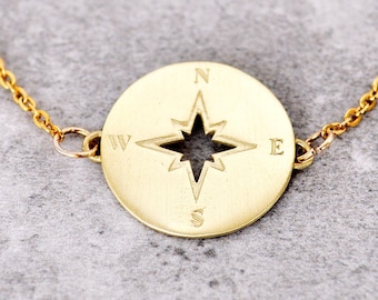 May include: Gold-colored bracelet featuring a round pendant with a compass design. The pendant has a star-shaped cutout in the center and directional markings for North, South, East, and West. The bracelet is made of a delicate chain.