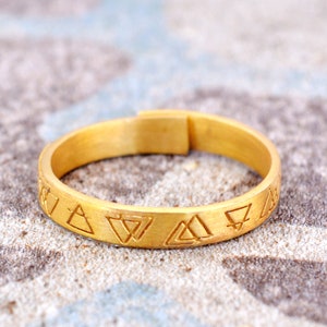 May include: A gold band ring with a repeating pattern of triangles engraved around the band.