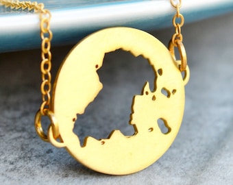 May include: A gold necklace with a pendant shaped like the outline of an island. The pendant is hanging on a delicate gold chain.