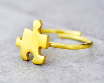 May include: A gold-colored ring with a puzzle piece design. The ring is simple and elegant.