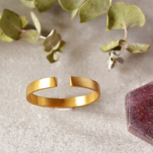 Puede incluir: Un anillo de oro con un espacio en la banda, mostrado sobre una superficie blanca con piedras preciosas púrpuras.