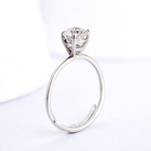 May include: A silver ring with a single, clear, round gemstone set in a prong setting.