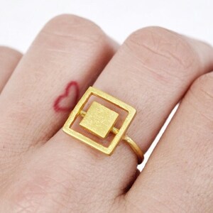 Puede incluir: Anillo de oro con un diseño cuadrado. El anillo se lleva en un dedo.